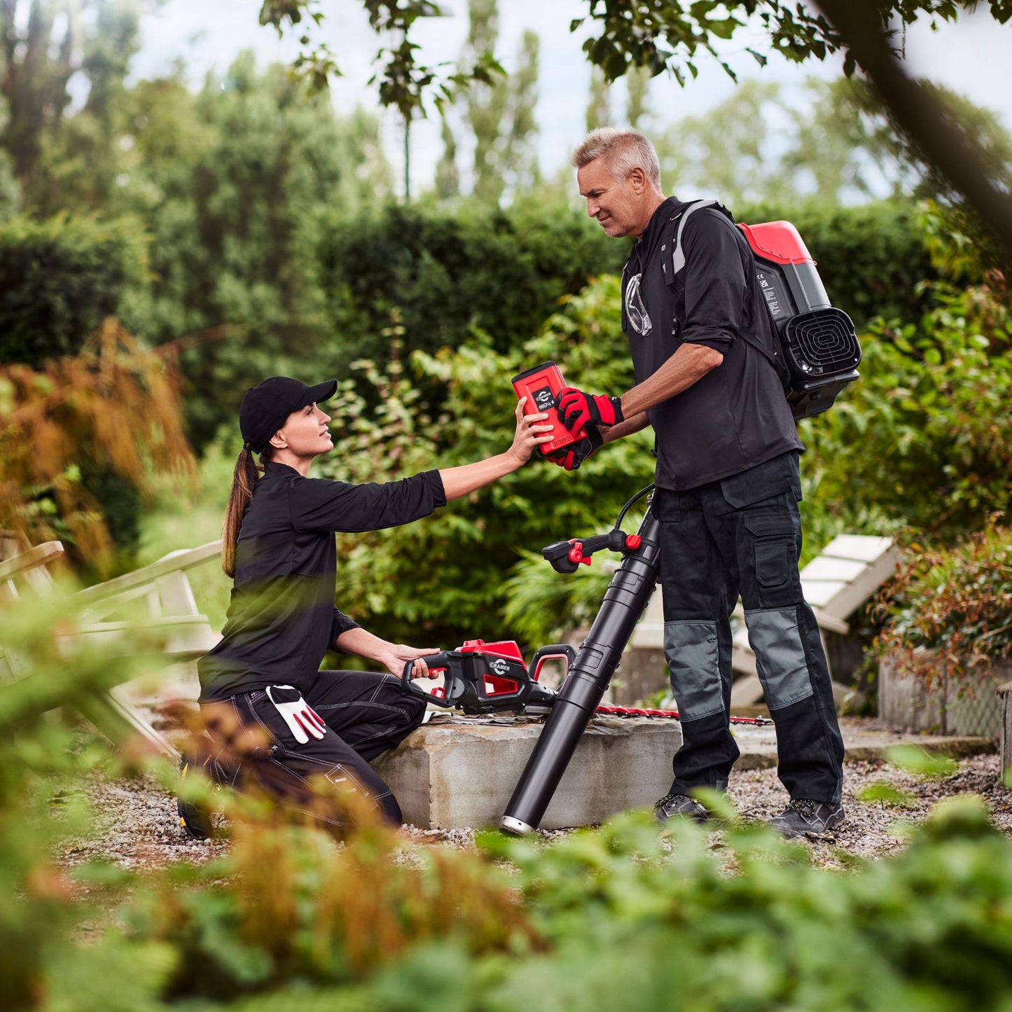 Two people in a garden setting with gardening tools and equipment.