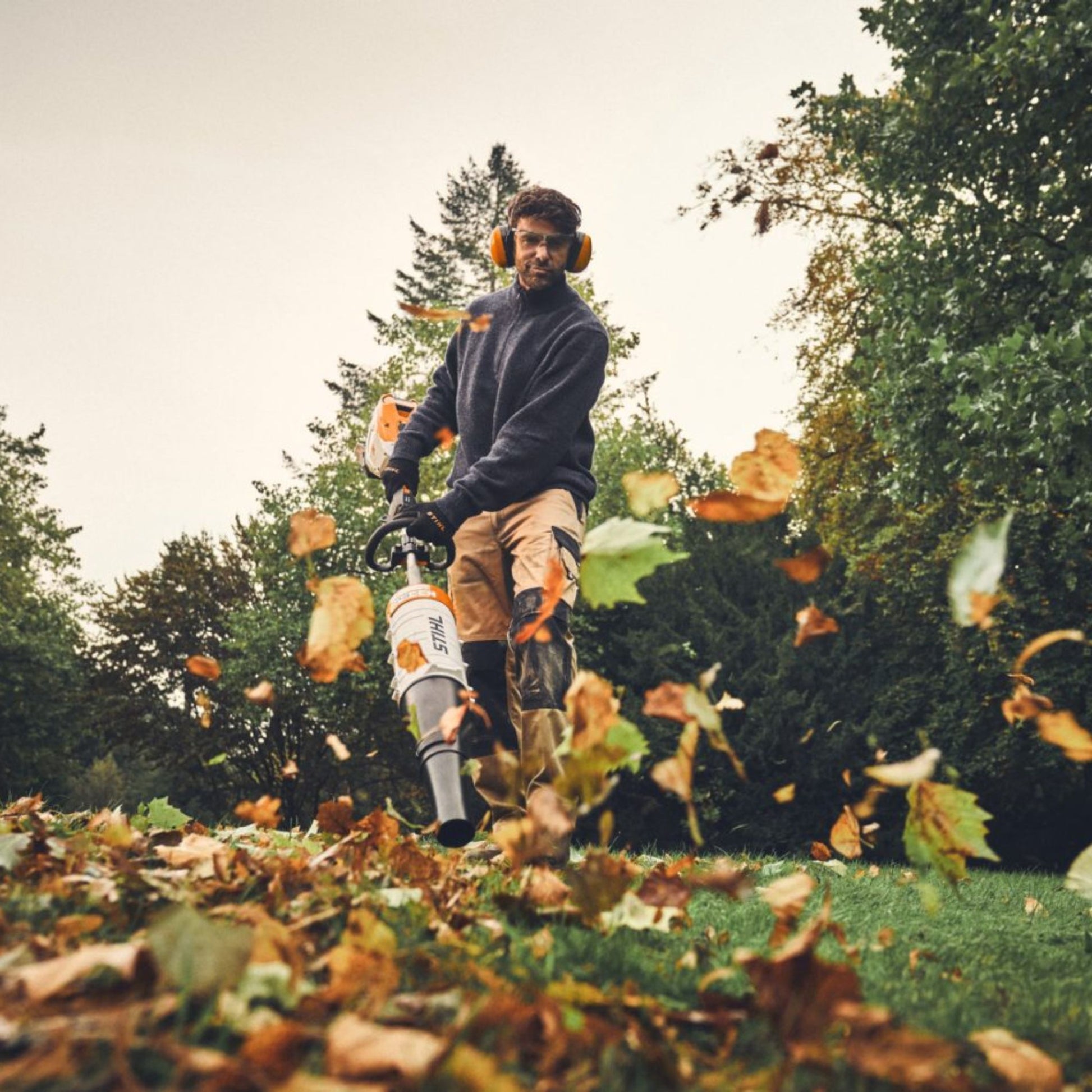 Person using a multi tool leaf blower to clear leaves from a lawn