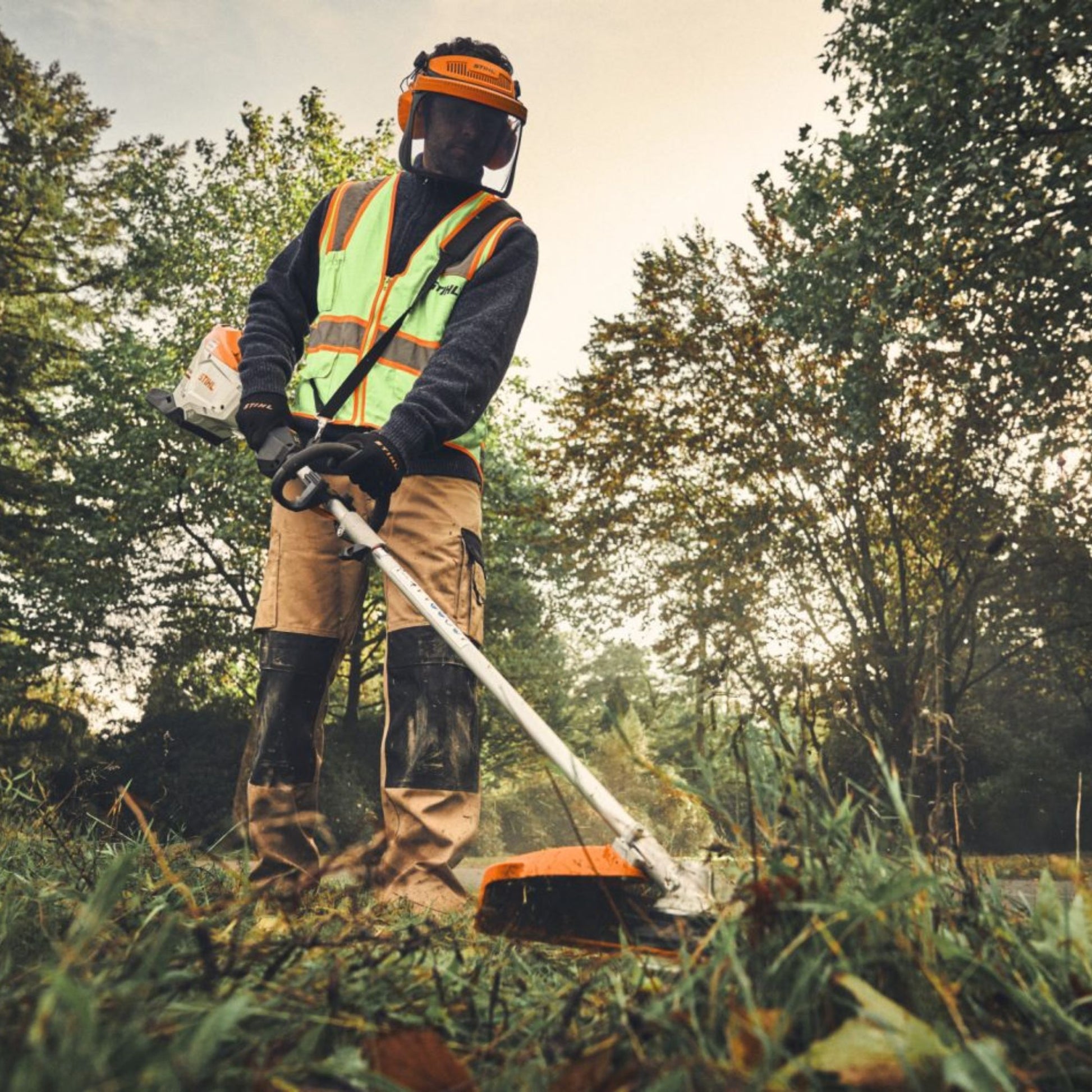 Person using a multi tool string trimmer in a wooded area