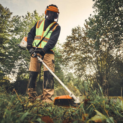 Person using a multi tool string trimmer in a wooded area