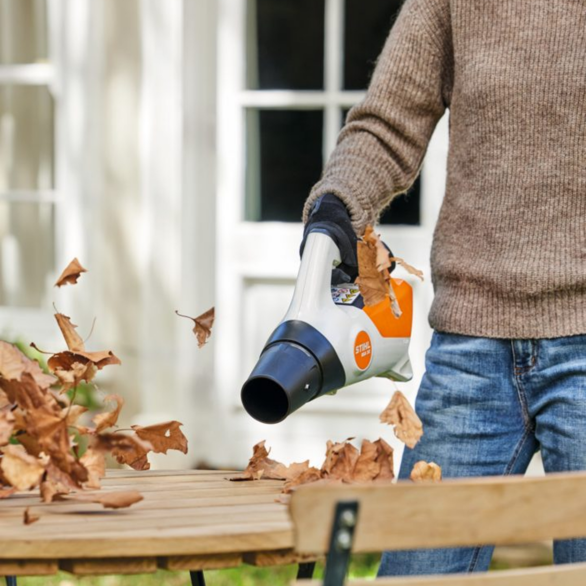 leaf blower being used to clear leaves from garden furniture