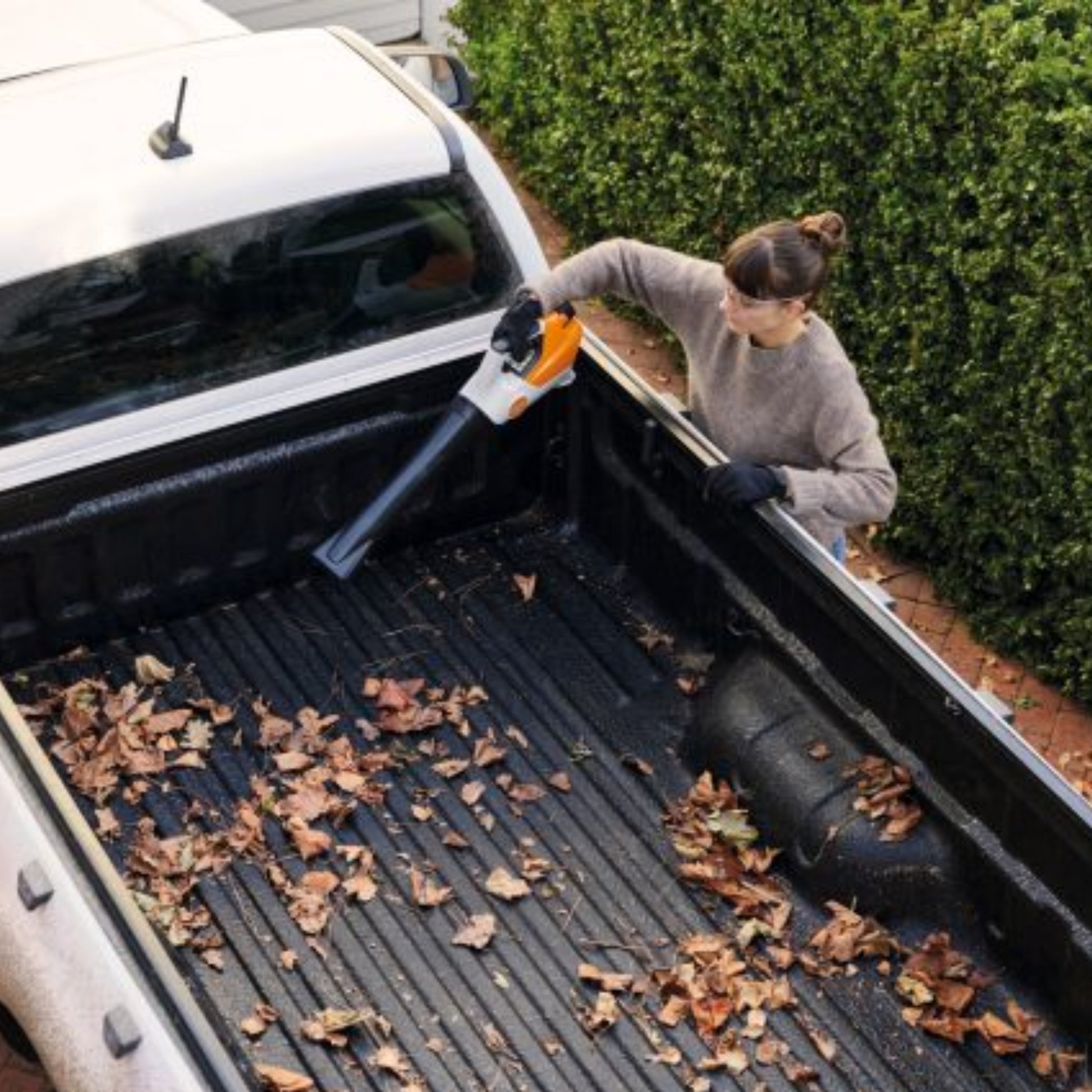 leaf blower being used to clear leaves from back of truck